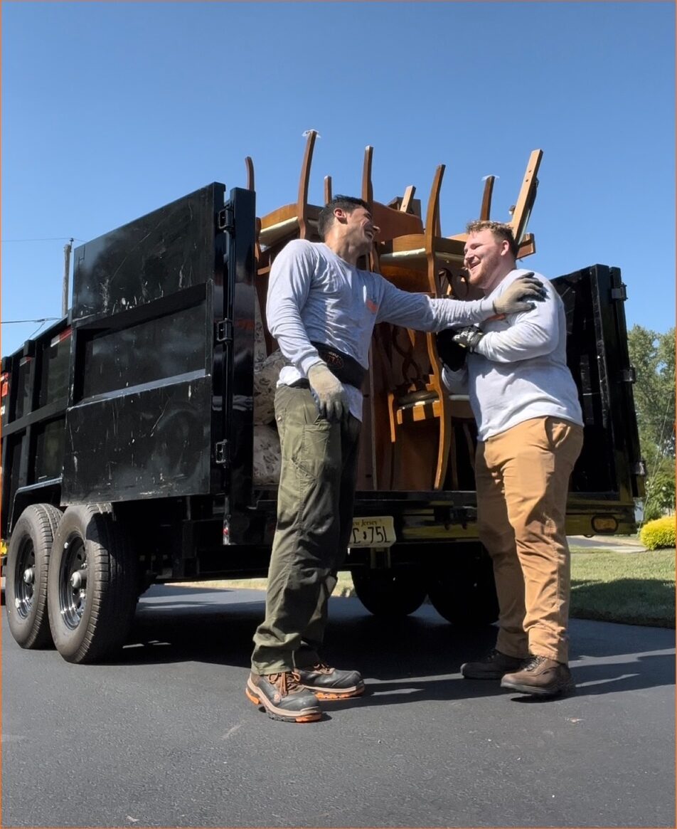 Two ExtraHands ASAP crew members carrying furniture out to the loaded trailer on a driveway